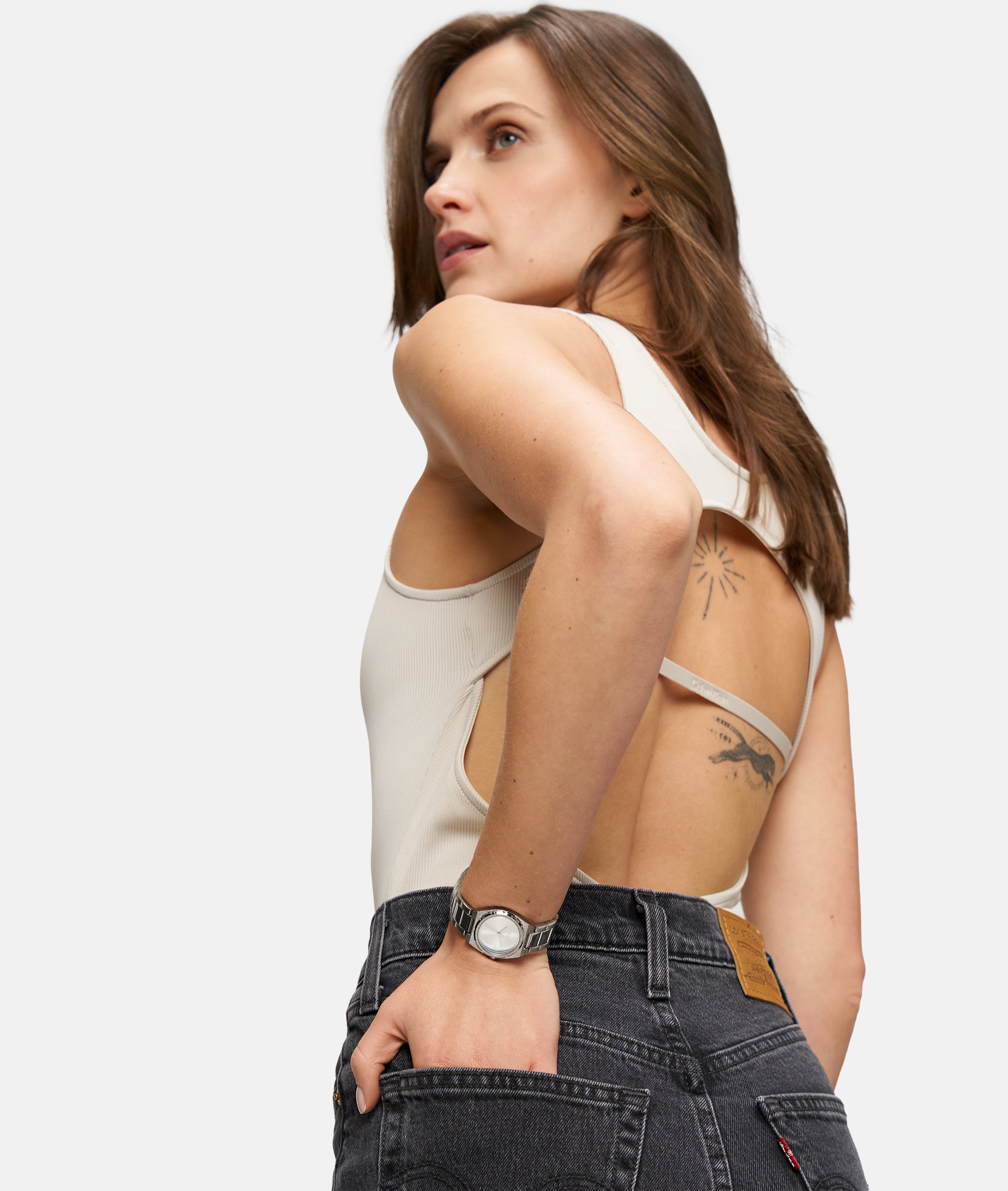 Frau in einem ärmellosen beigen Oberteil und schwarzen Jeans, mit Tattoos an Armen und Rücken, mit der Tamaris Armbanduhr - The Cool One von Tamaris.