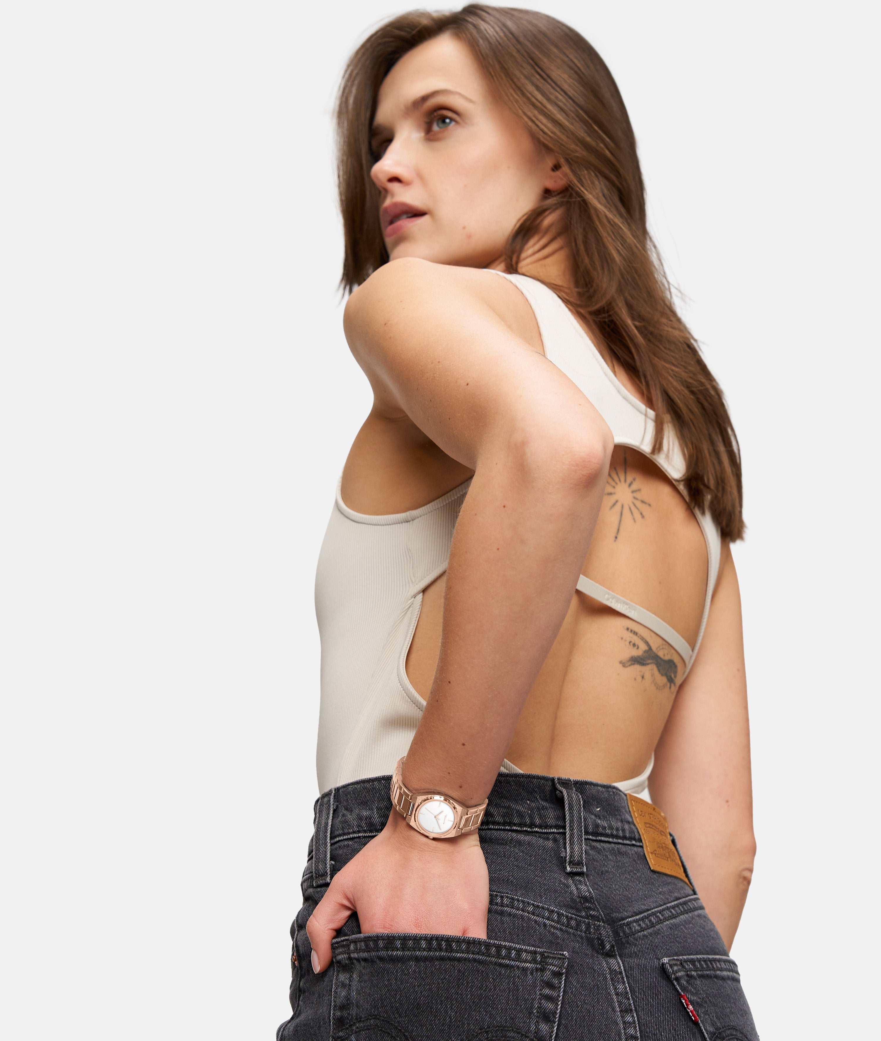 Frau in einem ärmellosen, rückenfreien Top und schwarzen Jeans, mit Tattoos und der Tamaris Armbanduhr - The Cool One von Tamaris, schaut zur Seite.