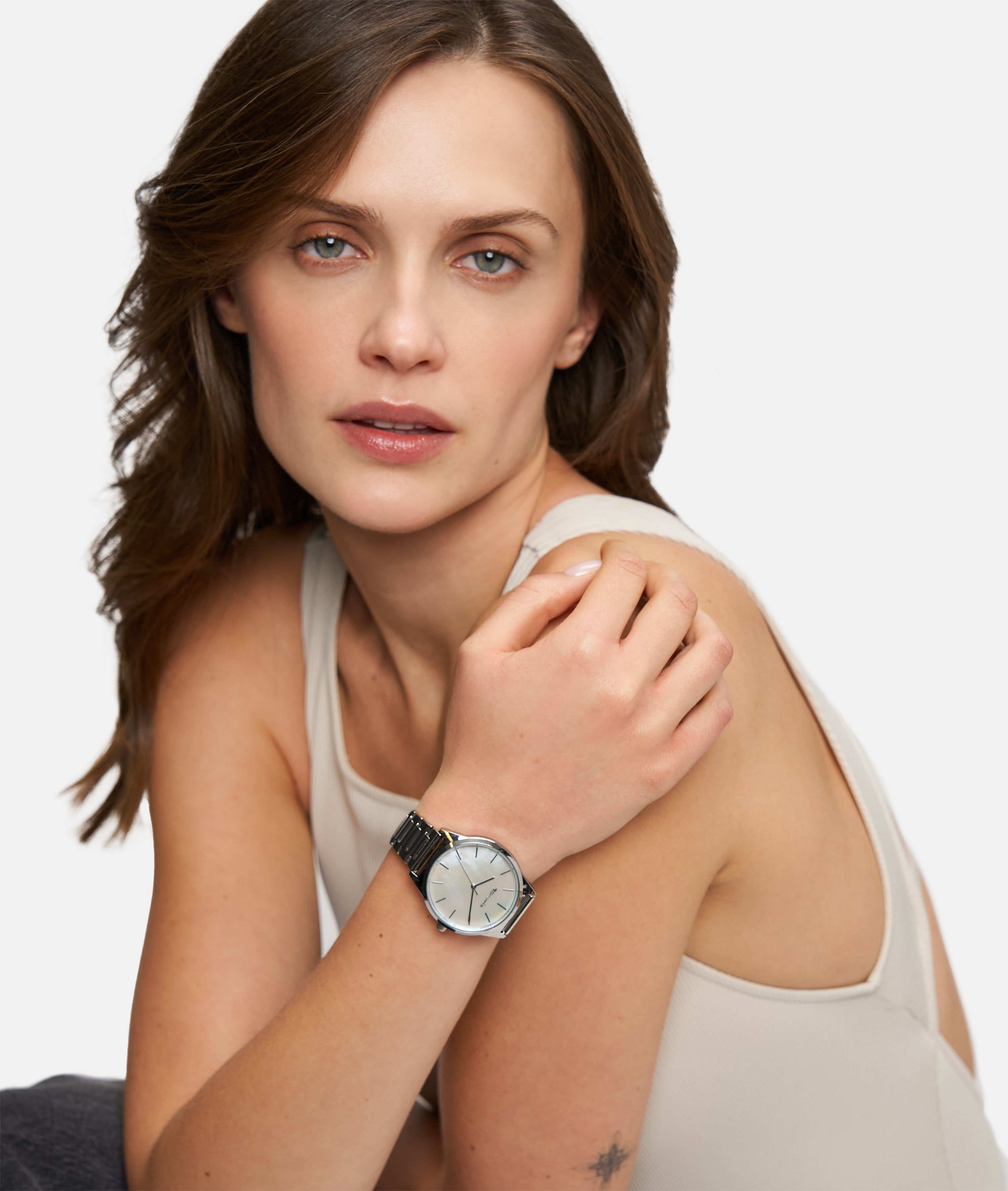 Eine Frau in einem beigen Tank-Top modelliert die Tamaris Armbanduhr - Basic Elegance mit einem eleganten Perlmuttzifferblatt und blickt in die Kamera vor einem schlichten Hintergrund.