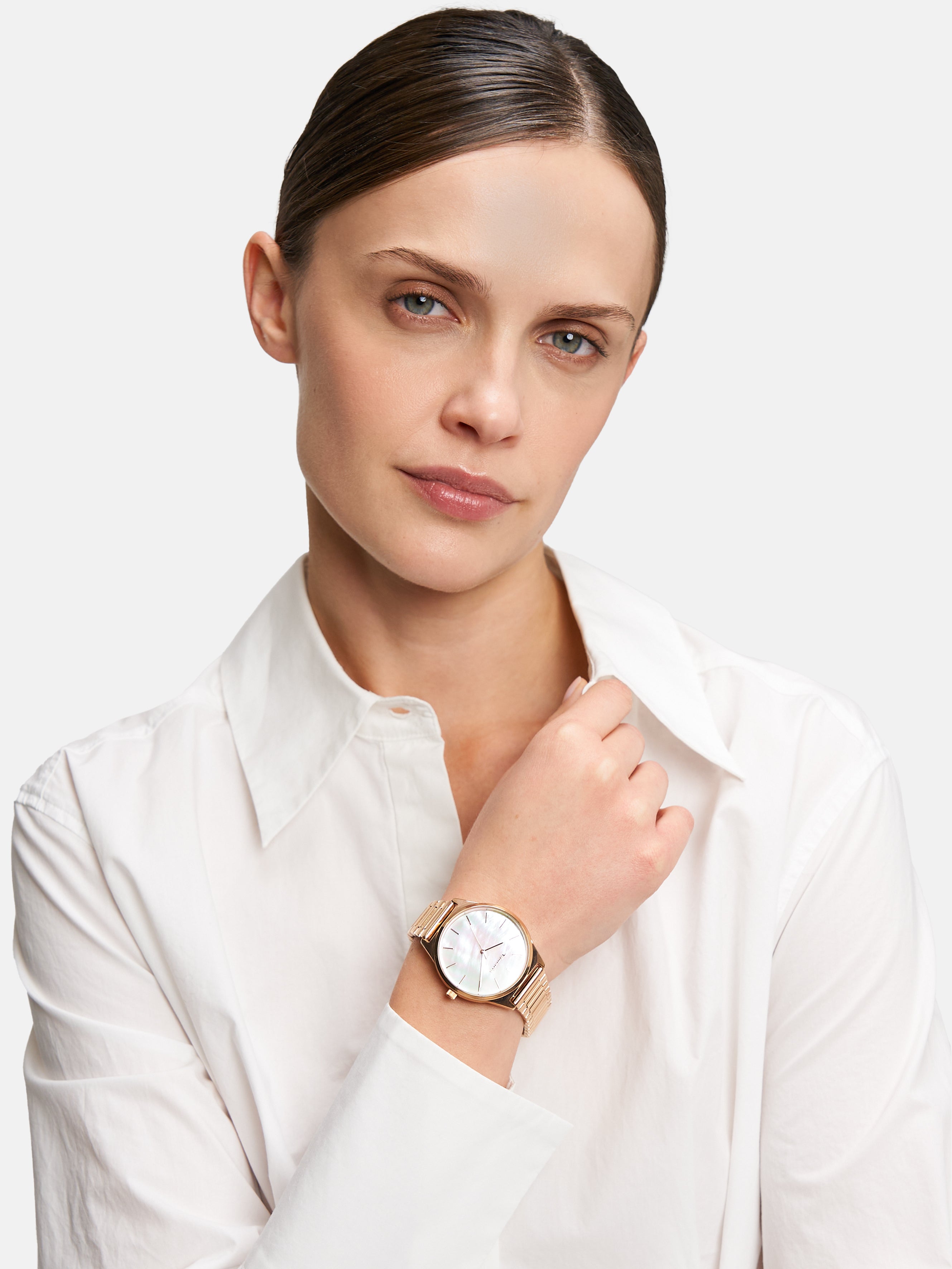 Frau in weißem Hemd, die eine Tamaris Armbanduhr - Basic Elegance mit Perlmutt-Zifferblatt trägt und mit neutralem Blick in die Kamera schaut.