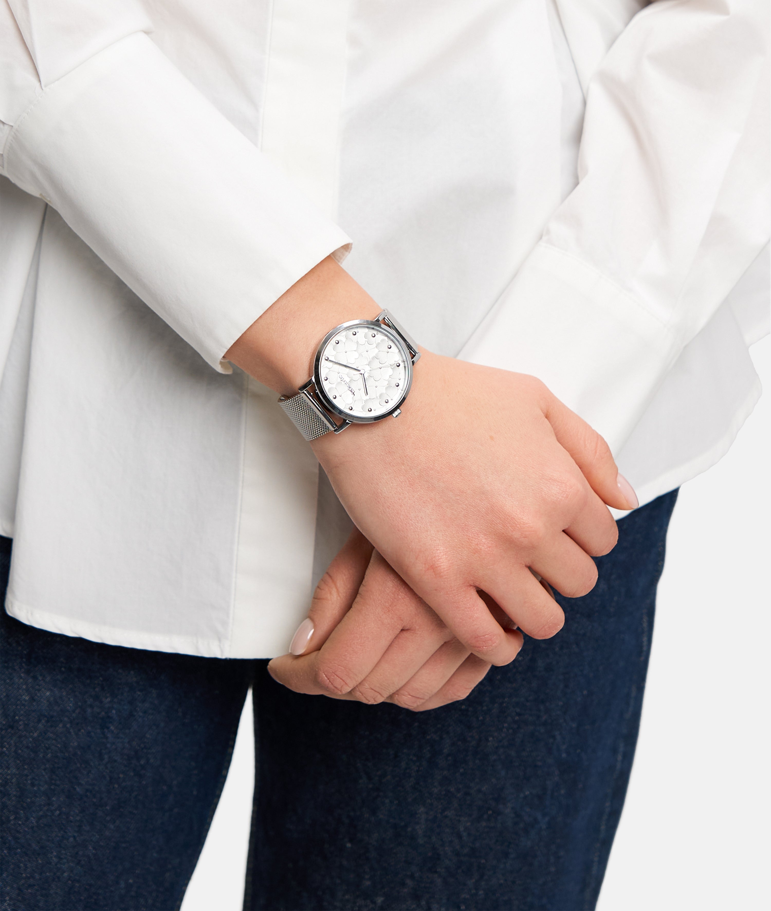 Eine Person in weißem Hemd und Jeans trägt die stilvolle Tamaris Armbanduhr - Clover, eine silberne Tamaris-Uhr mit weißem Zifferblatt und elegantem Netzband.