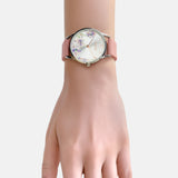 Eine Hand trägt die Tamaris Armbanduhr - The Flower von Tamaris mit einem rosafarbenen Silikonarmband und einem floralen Ziffernblattdesign vor einem hellen Hintergrund.