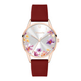 Die Tamaris Armbanduhr - The Flower von Tamaris kombiniert ein roségoldenes Gehäuse und ein rotes Silikonarmband mit einem silbernen Zifferblatt, das mit einem eleganten Blumendruck verziert ist.