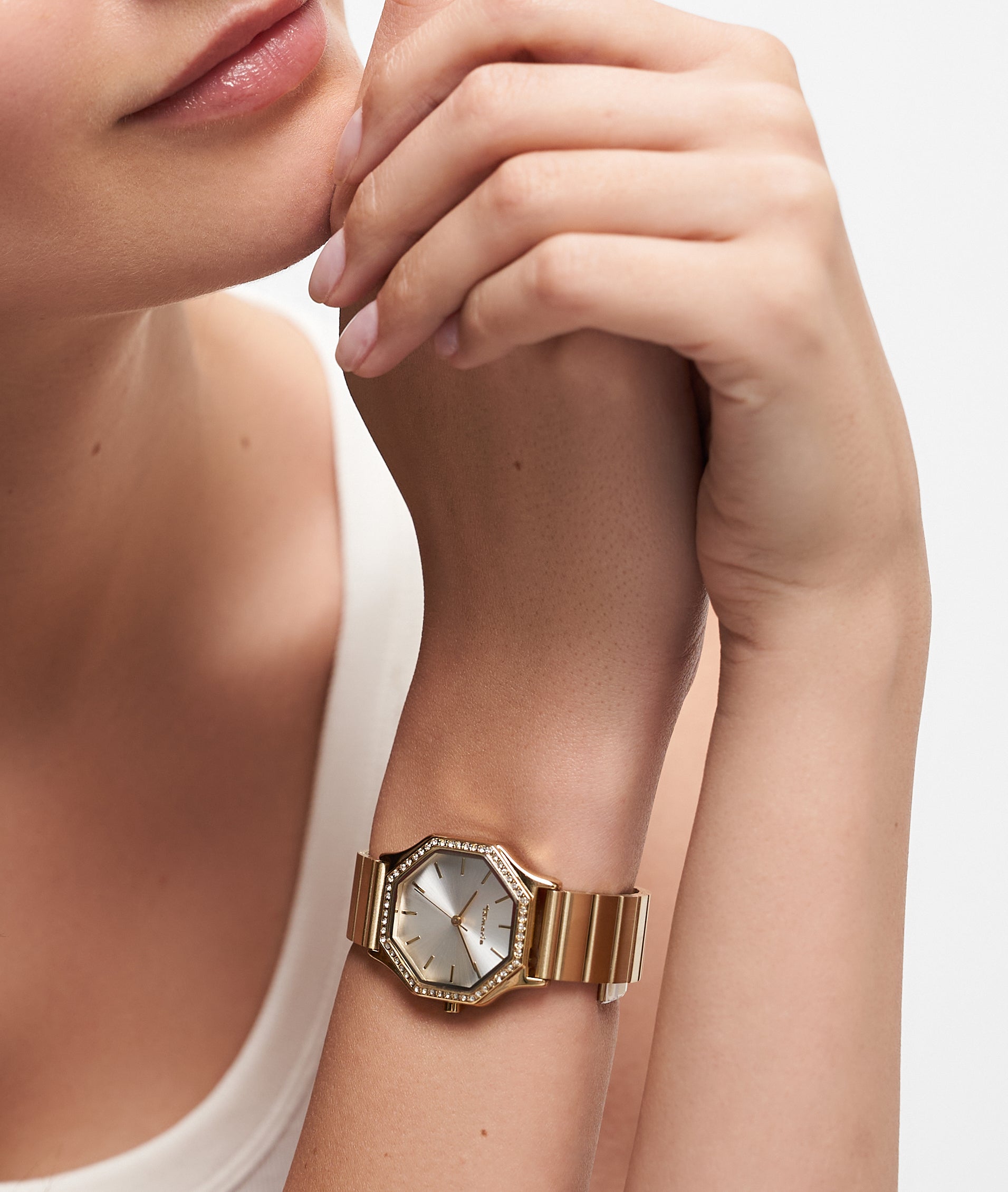 Eine Frau, die die Tamaris Armbanduhr - Sparkling Octavia mit einem goldenen sechseckigen Gesicht, Zirkoniasteinen und einem eleganten Edelstahlarmband trägt, stützt ihre Hand auf ihr Kinn.