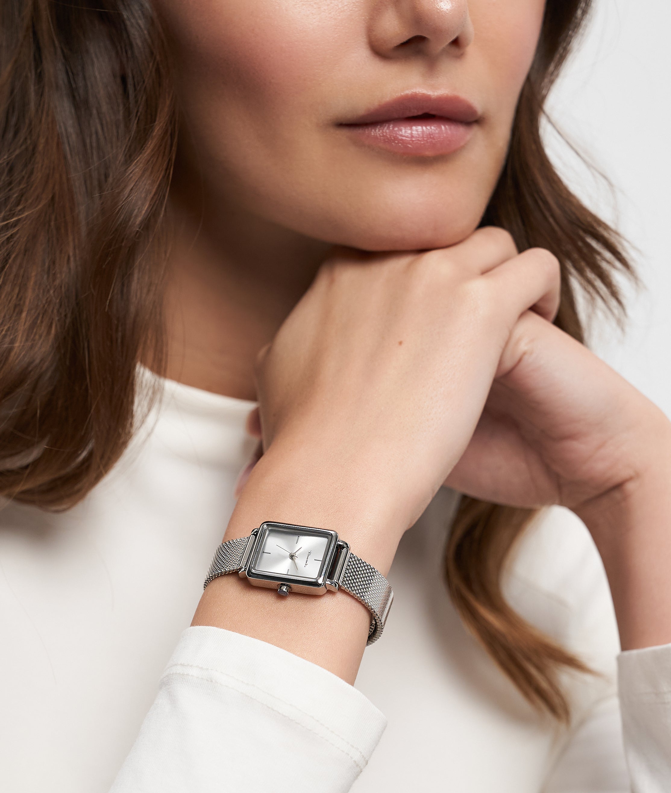 Eine Frau in einem weißen langärmeligen Oberteil, die die Tamaris Armbanduhr - Tiny Watch trägt, stützt ihr Kinn auf ihre Hände - ein Bild von minimalistischer Eleganz.