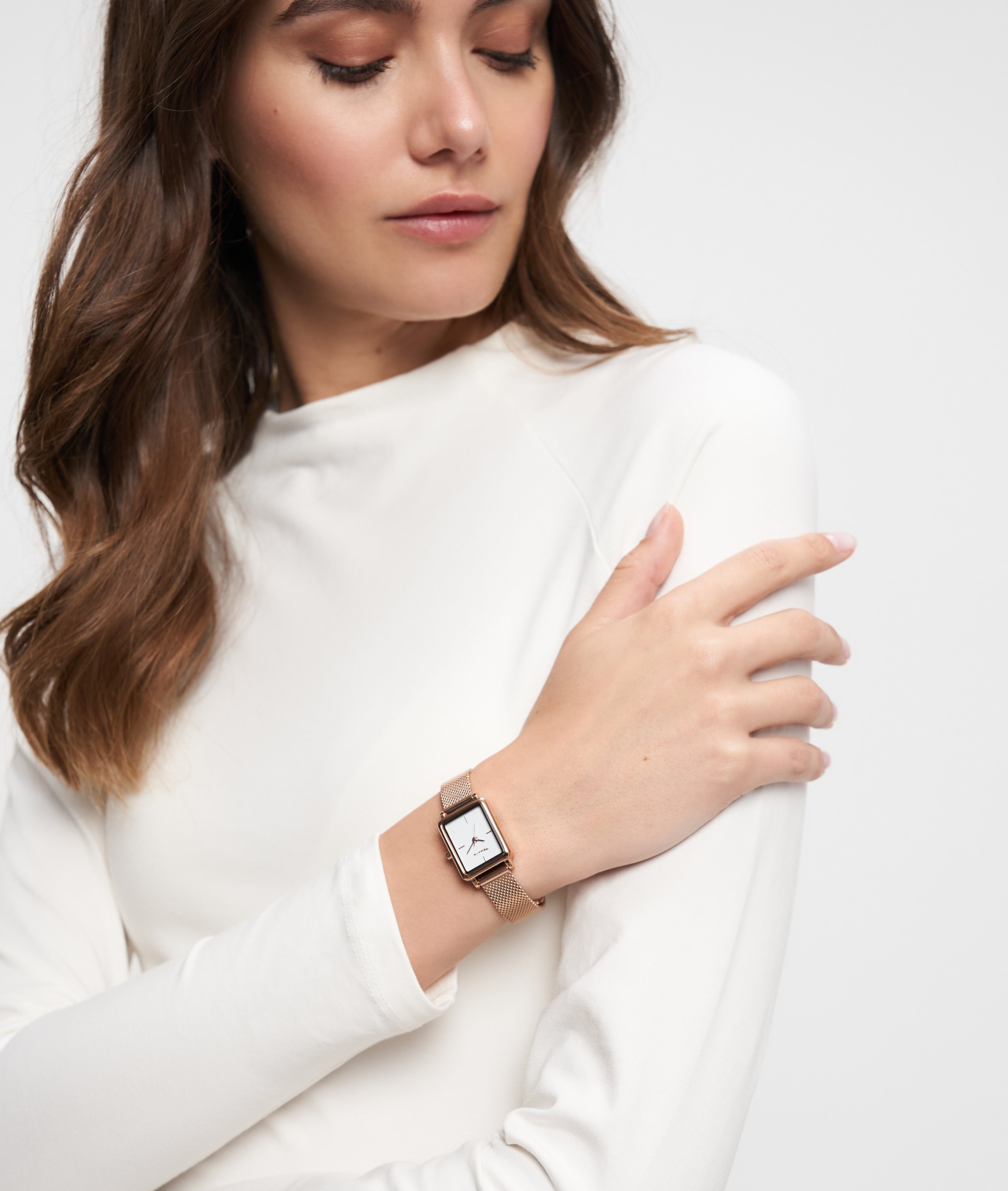 Eine Frau in einem weißen Oberteil blickt auf ihr Handgelenk und trägt die goldene Tamaris Armbanduhr - Tiny Watch von Tamaris, ein Statement von minimalistischer Eleganz.