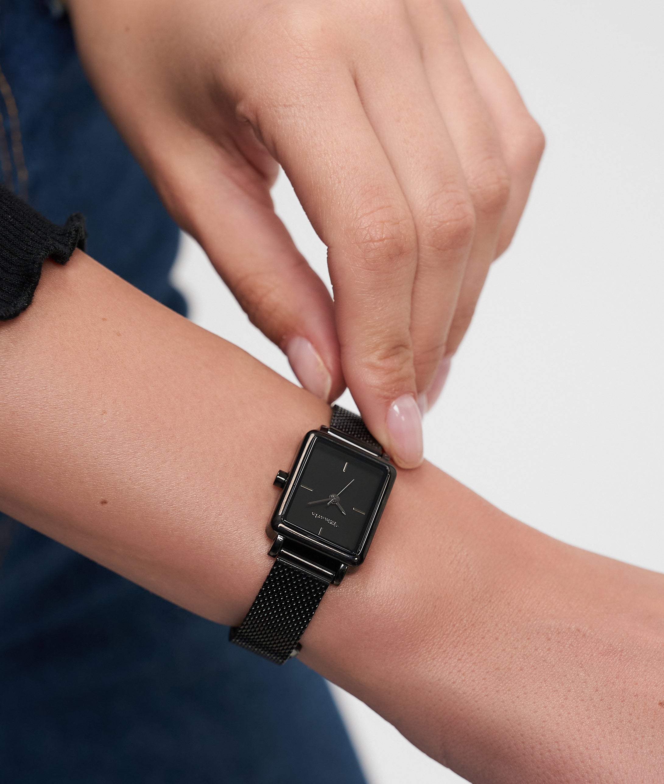 Eine Person trägt eine schwarze, quadratische Tamaris Armbanduhr - Tiny Watch von Tamaris an ihrem linken Handgelenk und unterstreicht damit die minimalistische Eleganz.