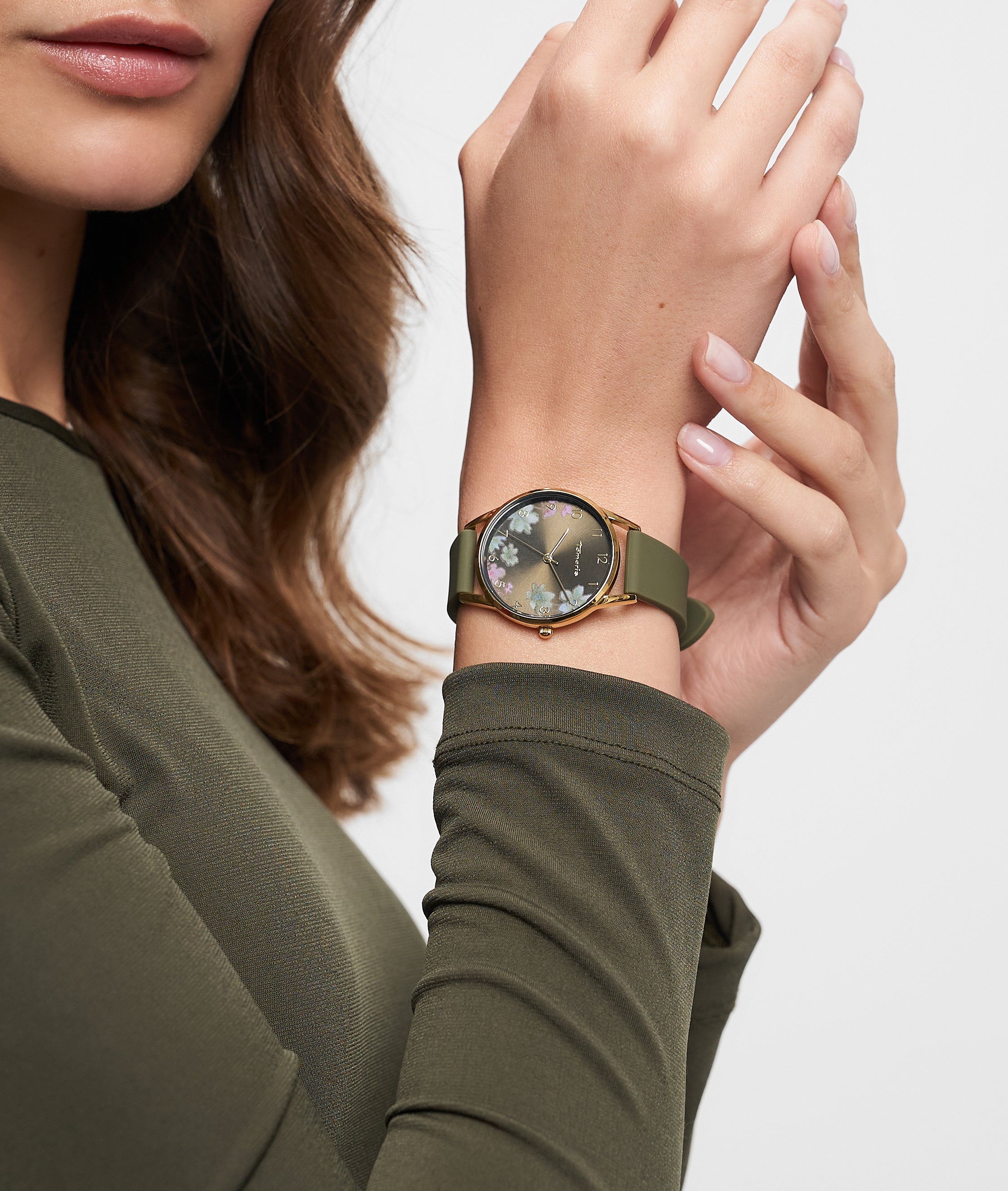 Eine Frau trägt ein olivgrünes langärmeliges Oberteil und eine Tamaris Armbanduhr - Sporty Flowers von Tamaris mit Blumenmotiv und grünem Silikonband am Handgelenk.