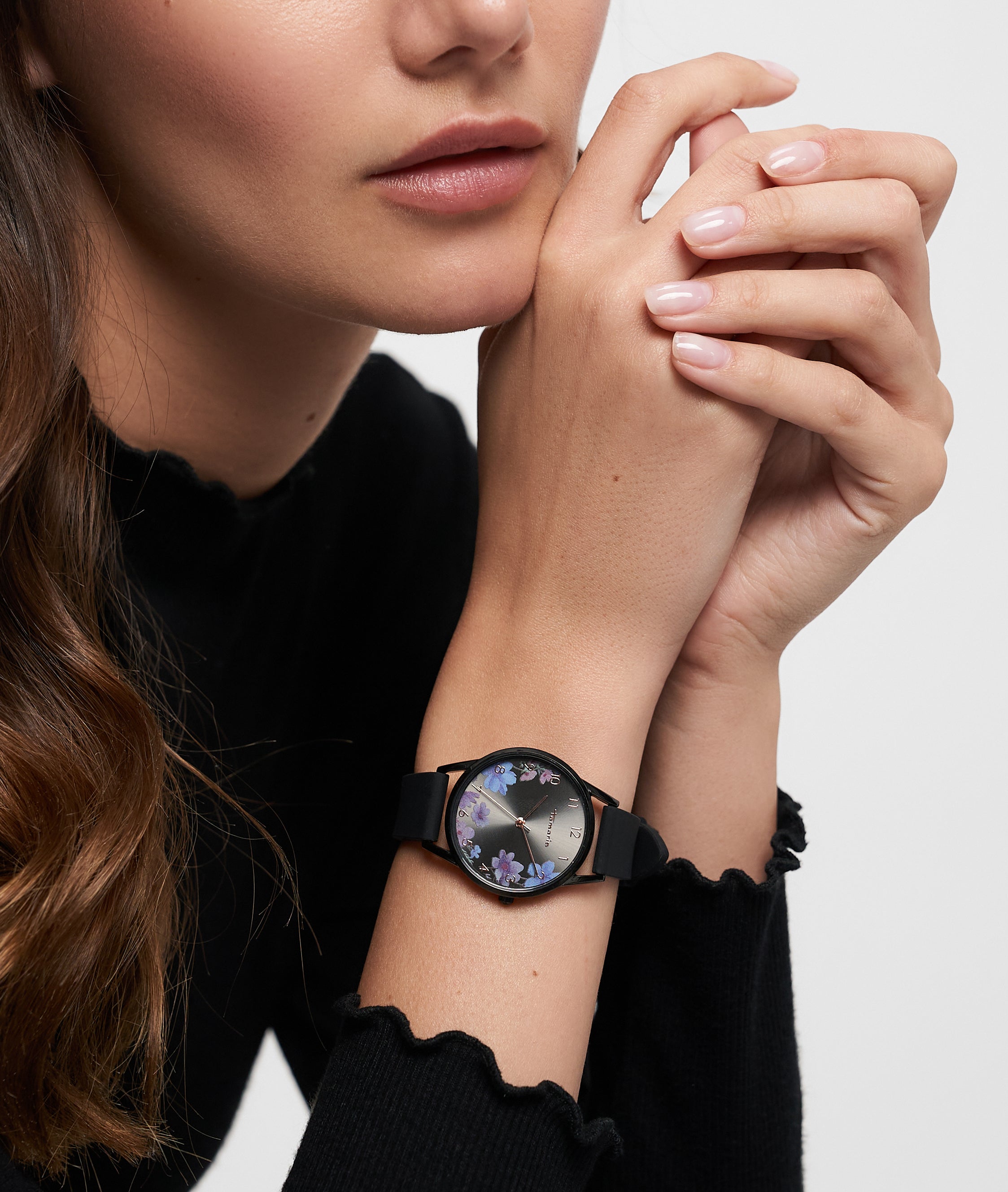 Eine Frau in einem schwarzen Oberteil, die Hände am Kinn verschränkt, trägt die Tamaris Armbanduhr - Sporty Flowers von Tamaris mit ihrem floralen Design und dem sportlichen Silikonband.