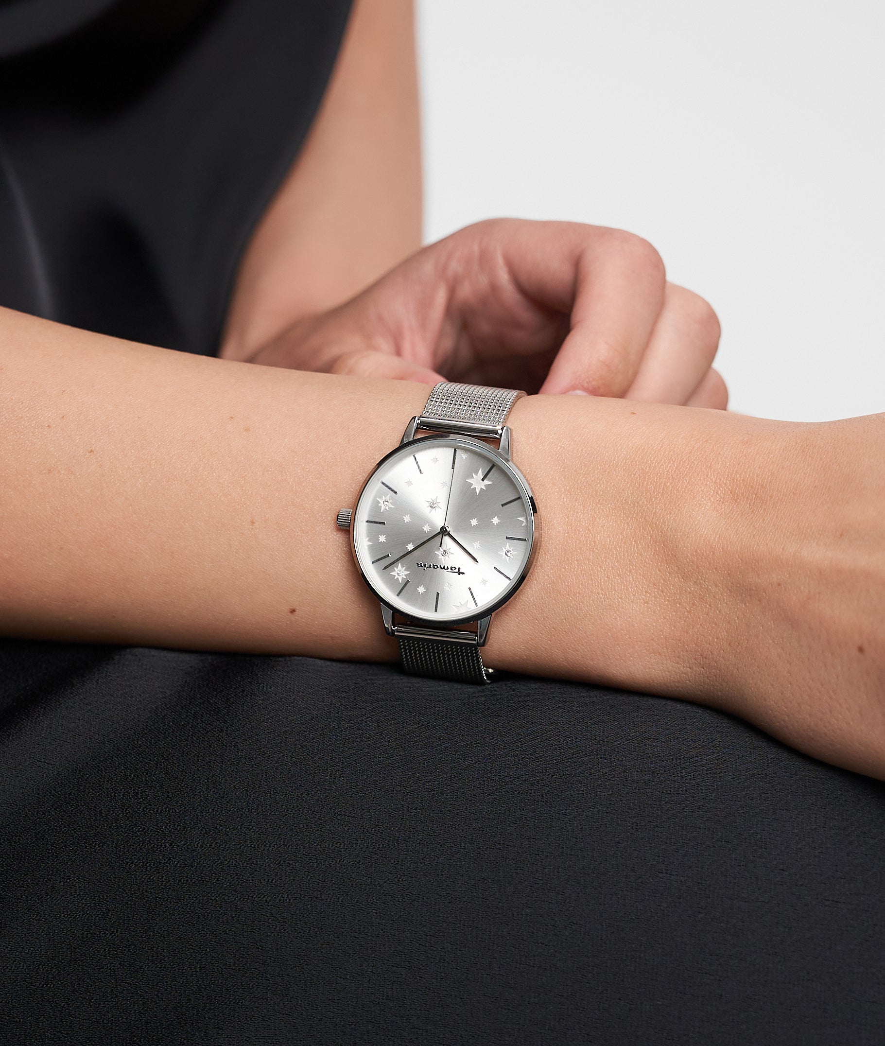 Die Tamaris Armbanduhr - Shiny Stars von Tamaris verleiht mit ihrem silbernen Netzband einem schwarzen Outfit einen Hauch von Eleganz und modernem Stil.