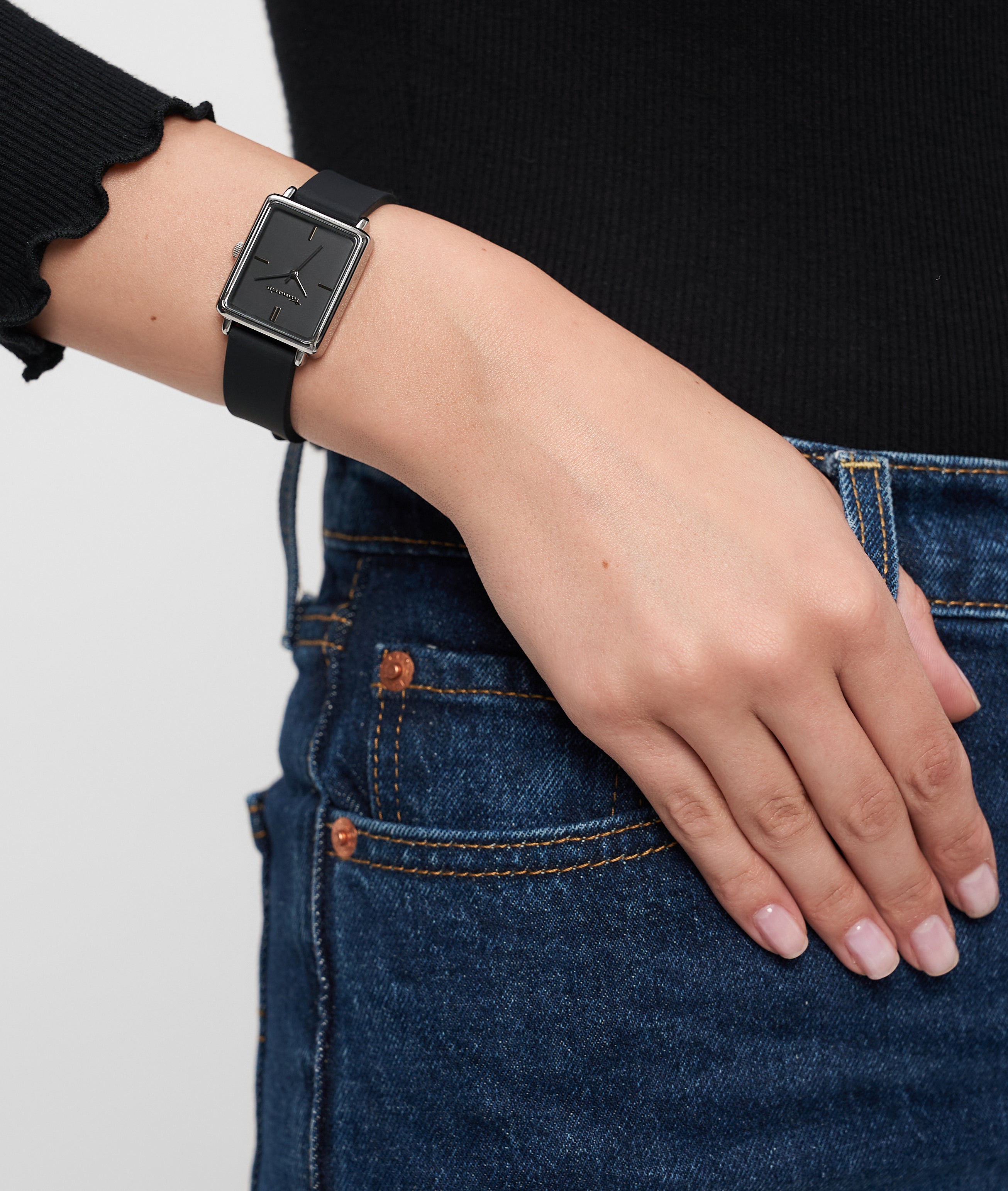 Eine Person, die die Tamaris Armbanduhr - The Silicon Square von Tamaris mit schwarzem Silikonband und blauer Jeans trägt, stützt ihre Hand auf die Hüfte.