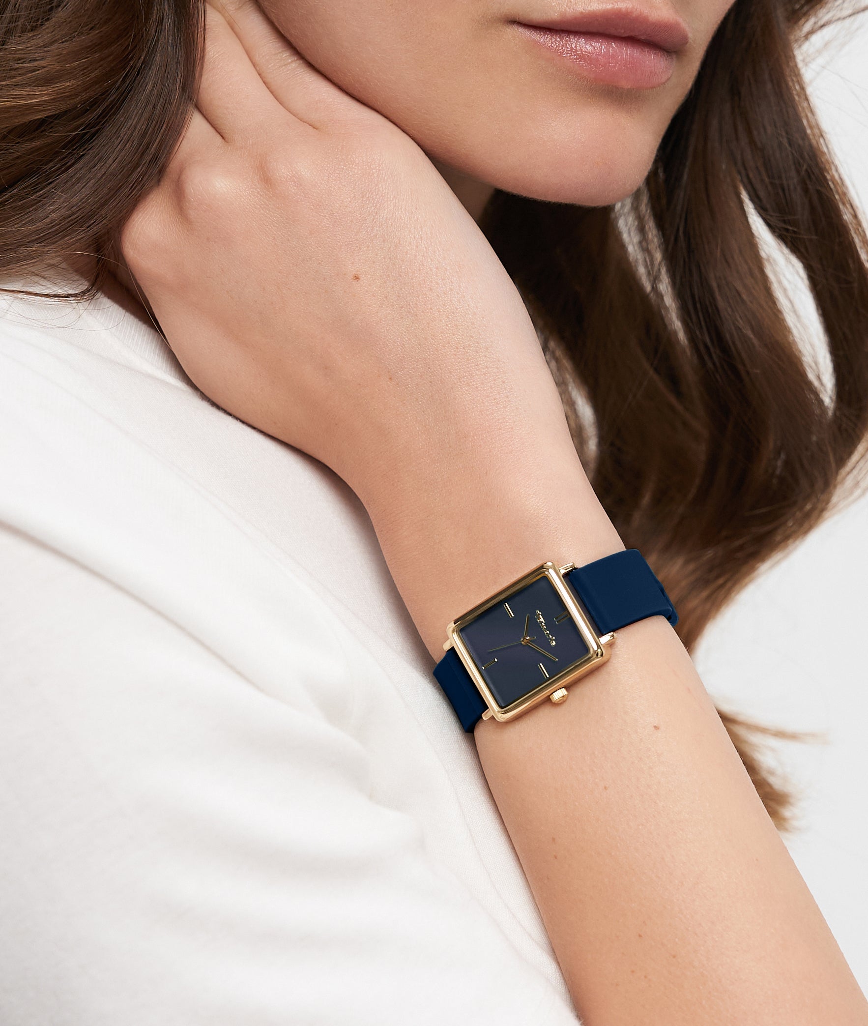 Eine Frau trägt die Tamaris Armbanduhr - The Silicon Square mit einem quadratischen goldenen Gehäuse und einem marineblauen Silikonarmband am linken Handgelenk.