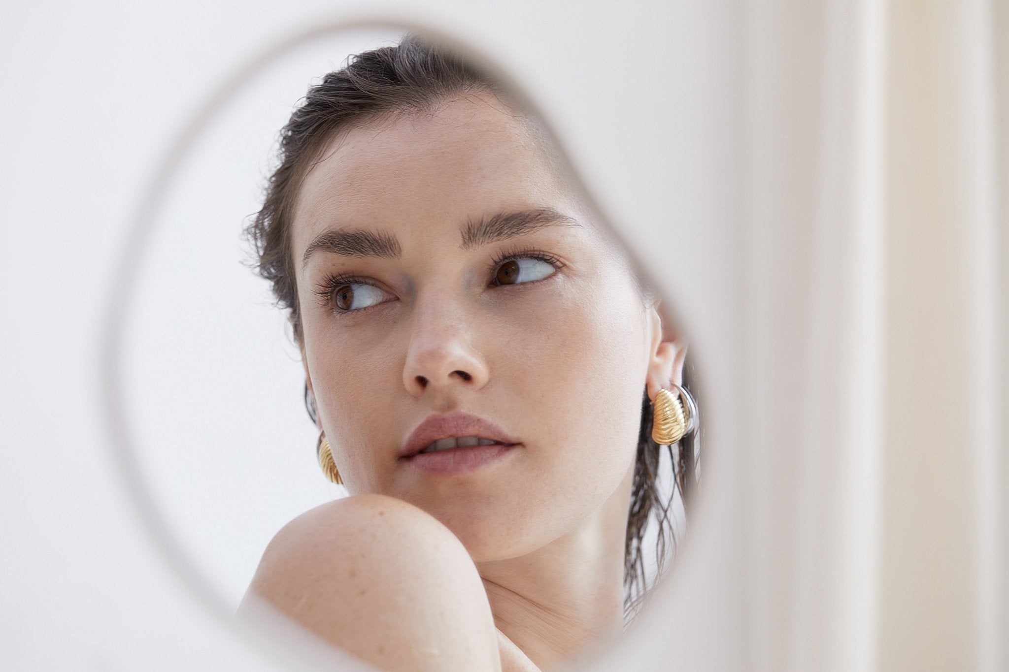 Frau mit goldenen Echtzeit-Creolen im Spiegelbild – moderner Schmuck trifft auf zarte Eleganz und minimalistisches Design.