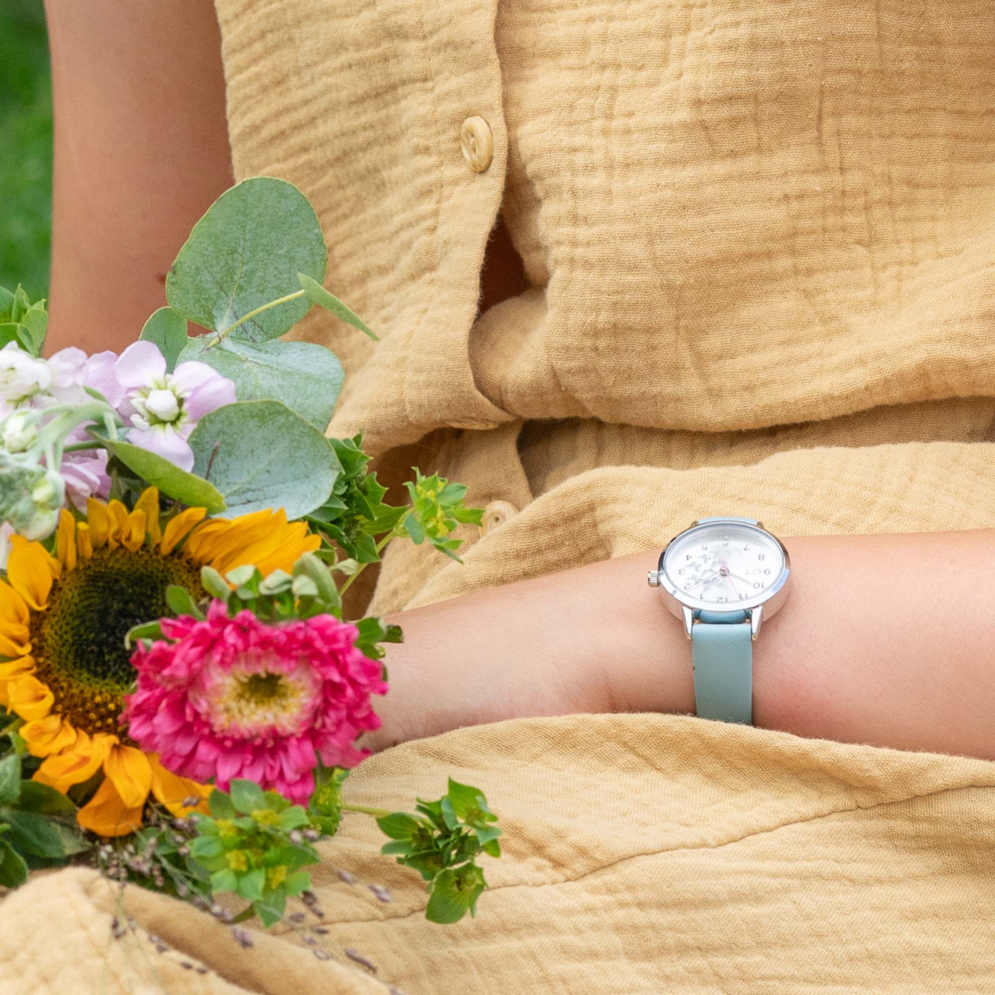 Cool Time Kids Armbanduhr mit einem silbernen Zifferblatt mit glitzernden Schmetterlingen, silbernem Gehäuse und blauem Kunstlederband; Tragebild