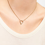 Nahaufnahme des goldenen Dreiecks-Anhängers an der LIEBESKIND BERLIN Halskette - The Iconic von Liebeskind Berlin, getragen mit einem cremefarbenen Top - ein schickes Accessoire für mühelose Eleganz.