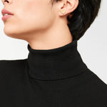 Person trägt einen schwarzen Rollkragenpullover und goldene Ohrstecker in Herzform, gepaart mit dem LIEBESKIND BERLIN Set - Broken Heart von Liebeskind Berlin, von den Schultern aufwärts gezeigt.