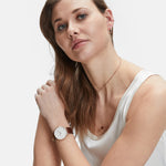 Frau in einem weißen Tank-Top, die eine Armbanduhr, mehrere Ketten und die LIEBESKIND BERLIN Ear Cuff - The Small Basic Logo by Liebeskind Berlin trägt und in die Kamera schaut.