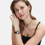 Frau mit hellbraunem Haar trägt ein schwarzes Tanktop, Uhr, Halskette und die LIEBESKIND BERLIN Ear Cuff - The Small Basic Logo by Liebeskind Berlin, wobei sie ihr Ohr berührt und nach vorne schaut.