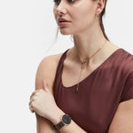 Frau in einem ärmellosen weinroten Oberteil, trägt eine Halskette, eine elegante schwarze Armbanduhr und die LIEBESKIND BERLIN Ear Cuff - The Small Basic Logo by Liebeskind Berlin, mit Blick zur Seite.