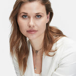 Eine Frau mit langen hellbraunen Haaren in einem weißen Blazer blickt in die Kamera. Sie trägt die LIEBESKIND BERLIN Ear Cuff - The Small Basic Logo von Liebeskind Berlin, die einen modernen, eleganten Touch vor einem schlichten Hintergrund hat.