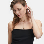 Frau in einem schwarzen ärmellosen Kleid, die eine goldene Halskette und die LIEBESKIND BERLIN Ear Cuff - The Small Basic Logo von Liebeskind Berlin trägt, blickt nach unten und berührt mit einer Hand ihr Ohr.