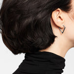 Eine Frau mit kurzen dunklen Haaren trägt ein schwarzes Oberteil und die LIEBESKIND BERLIN Creole - The Iconic Geometric Ohrringe von Liebeskind Berlin, die ein elegantes V-förmiges Design aufweisen.