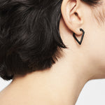 Close-up of a persons ear with short dark hair, wearing a black LIEBESKIND BERLIN Creole – The Iconic Geometric earring. The background is plain white.