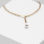 Die LIEBESKIND BERLIN Halskette - The ShortPearl von Liebeskind Berlin ist eine Goldkette im Gliederketten-Stil mit einem großen weißen Perlenanhänger, variabel verstellbar, dargestellt auf einer weißen geometrischen Fläche.