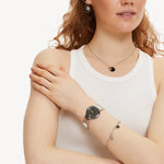 Tamaris Armbanduhr mit schwarzem Zifferblatt, silbernem Gehäuse mit kreisförmig angeordnetem Logoschriftzug auf schwarzer Epoxidlacklünette und silbernem Edelstahlband Tragebild