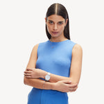 Eine Frau in einem ärmellosen blauen Top posiert mit verschränkten Armen, trägt eine Armbanduhr und schlichten Schmuck, darunter die Liebeskind Berlin Halskette - The Organic Twist für einen schicken Lagenlook.
