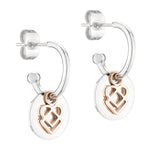 Die LIEBESKIND BERLIN Creole - Keep Loving Silberohrringe von Liebeskind Berlin sind mit roségoldenen Herzanhängern versehen, die an runden Scheiben auf weißem Hintergrund hängen.