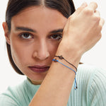 Eine Frau mit langen braunen Haaren trägt ein hellblaues Oberteil und zwei Kettenarmbänder - darunter das LIEBESKIND BERLIN Armband - Keep Loving von Liebeskind Berlin - für einen schicken Lagenlook.
