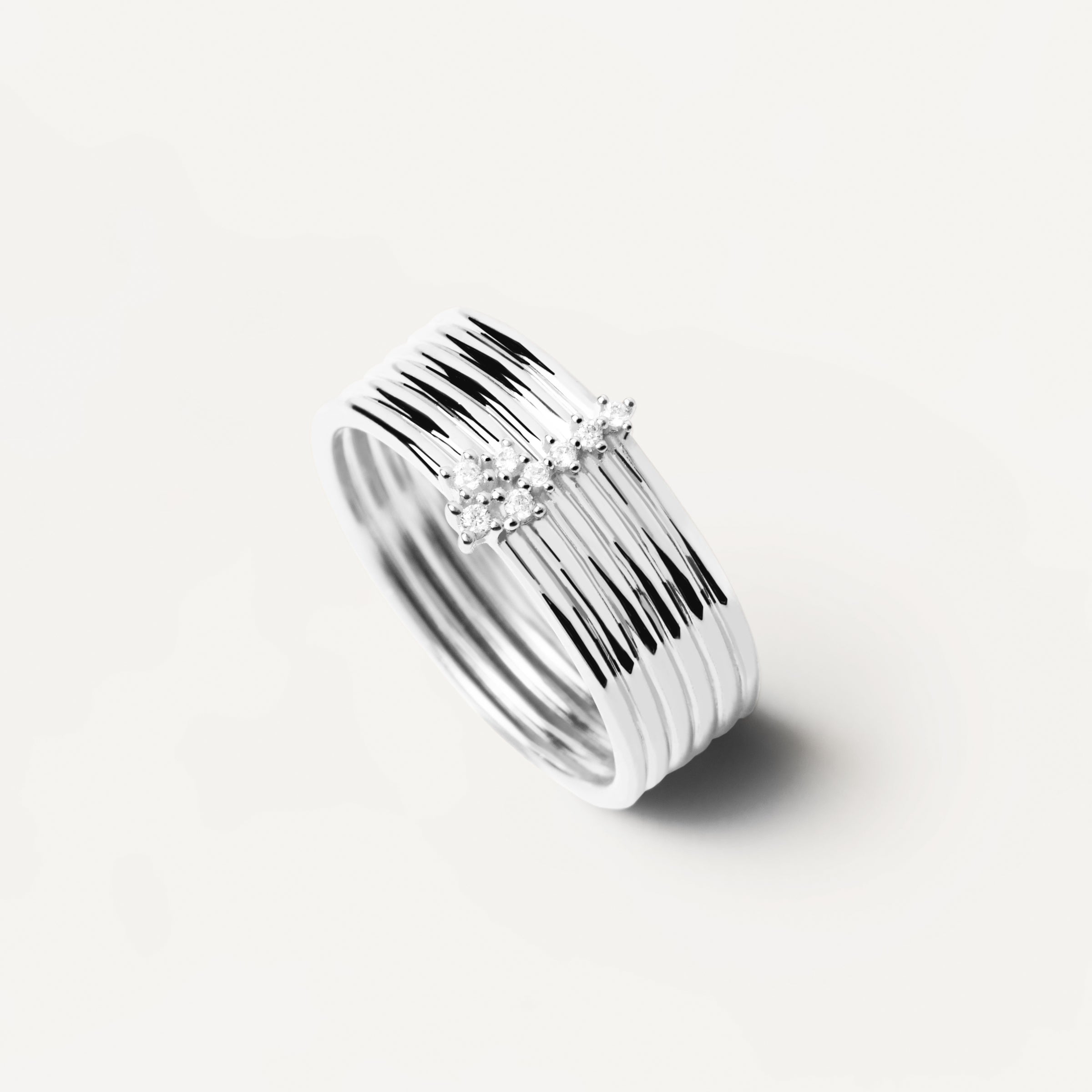 Der PDPaola Ring - Layered Rings in 52 von PDPaola besteht aus mehreren dünnen Silberbändern mit einem kleinen Cluster aus klaren Edelsteinen, die sich elegant vor einem weißen Hintergrund abheben.