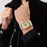 Philipp Plein Armbanduhr im Tonneau Shape mit teilskelettiertem silbernem Zifferblatt mit goldenem glassteinbesetztem Totenkopf- und Knochenmotiv, goldenem Gehäuse und weißem Edelstahlband Produktbild