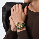 Mann in einem braunen Pullover, der die Philipp Plein Armbanduhr - The Golden Camouflage trägt und eine schwarze Jacke über der Schulter hält.