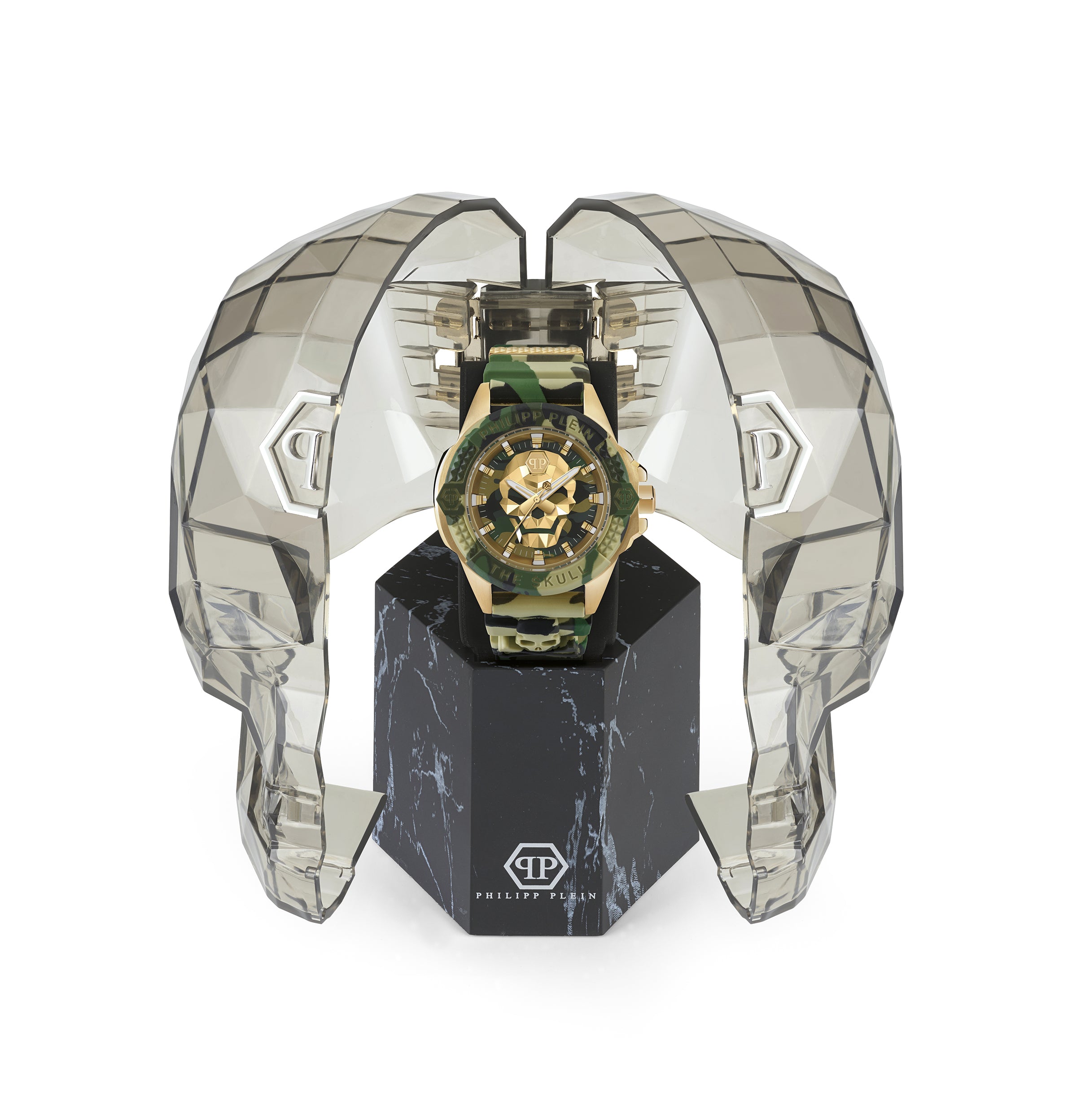 Die Philipp Plein Armbanduhr - The Golden Camouflage wird in einem transparenten, facettierten Gehäuse in Form eines Totenkopfes aus der Skull-Kollektion präsentiert, das auf einem schwarzen Marmorsockel ruht.