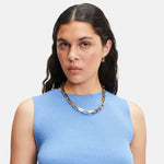 Frau mit langen dunklen Haaren in einem blauen ärmellosen Oberteil. Sie trägt die Liebeskind Berlin Halskette - Big Link mit goldener Kette und Ohrringen.