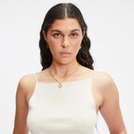 Eine Frau mit langen dunklen Haaren in einem weißen Tanktop trägt Goldschmuck und LIEBESKIND BERLIN Ohrhänger - Colorful Icon by Liebeskind Berlin und schaut ernst in die Kamera.