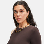 Frau mit gewelltem dunklem Haar trägt ein braunes Oberteil, eine goldene Halskette, Edelstahlohrringe und die Liebeskind Berlin Creole - Modern Elegance.