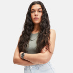 Eine Person mit langen gewellten Haaren steht selbstbewusst da, die Arme verschränkt, in einem ärmellosen Top und hellen Jeans, gestylt mit der Liebeskind Berlin LIEBESKIND BERLIN Halskette - Wear it Different.