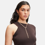 Frau mit langen dunklen Haaren, die ein braunes One-Shoulder-Top und die LIEBESKIND BERLIN Halskette - Wear it Different von Liebeskind Berlin trägt, schaut in die Kamera.