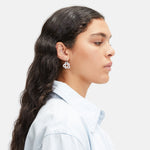 Frau im Profil mit langen dunklen Haaren, trägt ein hellblaues Hemd und bunte LIEBESKIND BERLIN Ohrhänger - Colorful Icon by Liebeskind Berlin.