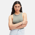 Frau mit langen dunklen Haaren in einem grauen Tank Top und hellen Jeans, trägt klobigen Silberschmuck und ein Liebeskind Berlin "Modern Elegance" Armband, Arme verschränkt.