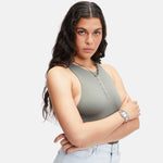 Frau mit langen gewellten Haaren in einem grauen ärmellosen Top und hellen Jeans, die Arme verschränkt, trägt das Liebeskind Berlin Armband - The Basic Trendy Chain und zeigt damit individuelles Design und einzigartigen Schmuckstil.