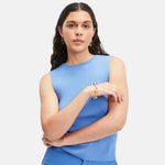 Eine Frau in einem ärmellosen blauen Top posiert selbstbewusst vor einem weißen Hintergrund und präsentiert das stilvolle Liebeskind Berlin Armband - Big Link, ein elegantes Damen Schmuckstück aus edlem Edelstahl.