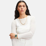 Frau mit weißem Top, Goldkette und der LIEBESKIND BERLIN Armbanduhr - The Classic Chronograph von Liebeskind Berlin mit Edelstahlgehäuse, steht mit verschränkten Armen vor einem hellen Hintergrund.