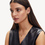 Frau mit glattem braunem Haar in einem schwarzen ärmellosen Oberteil trägt den LIEBESKIND BERLIN Ohrstecker - The Big Knot von Liebeskind Berlin und eine goldene Halskette, Blick zur Seite.