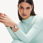 Eine Frau in einem hellblauen gerippten Oberteil posiert mit den Ohrsteckern The Big Knot von Liebeskind Berlin und schaut in die Kamera.