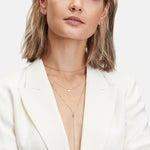 Frau in weißem Blazer trägt mehrlagige Goldketten, darunter die LIEBESKIND BERLIN Halskette - Gold Collection by Liebeskind Berlin, mit kleinen Reifohrringen; Bildausschnitt an den Schultern.