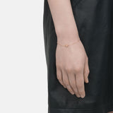 Eine Person trägt ein schwarzes Kleid und das Liebeskind Berlin LIEBESKIND BERLIN Set - Sparkling Rosé, bestehend aus einem zarten Roségoldarmband mit einem kleinen runden Anhänger, an ihrem Handgelenk.